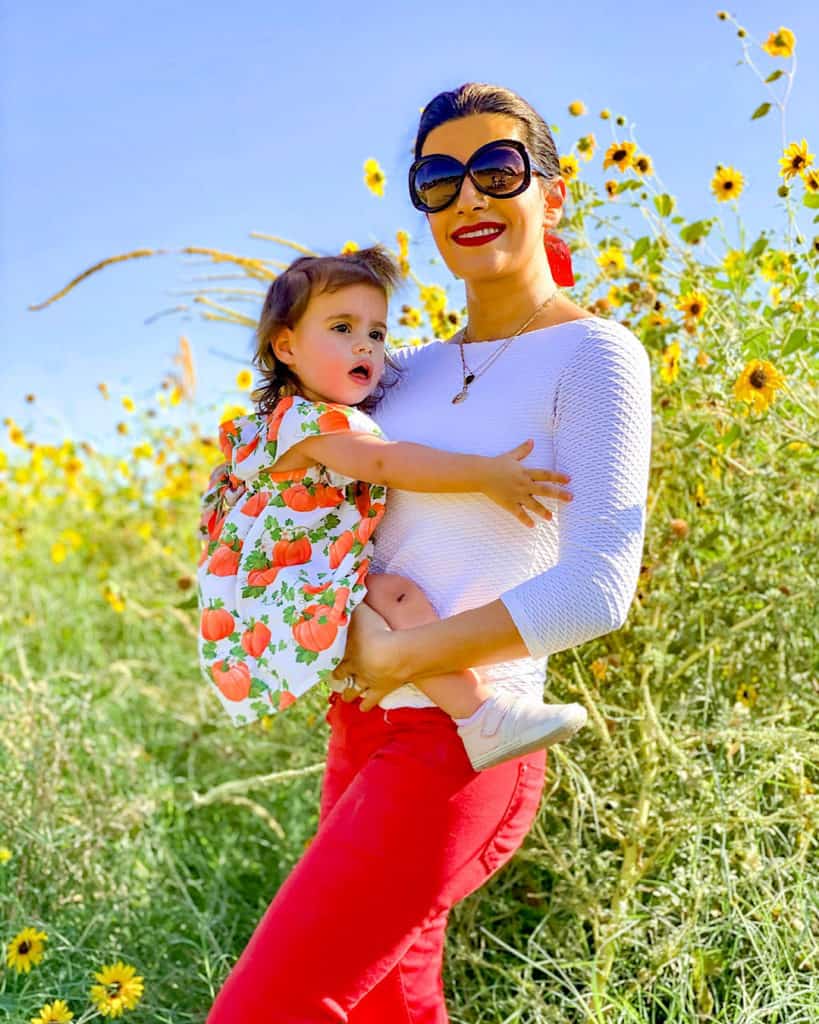 Taking your toddler to the pumpkin patch. Mom and daughter pose by sunflowers