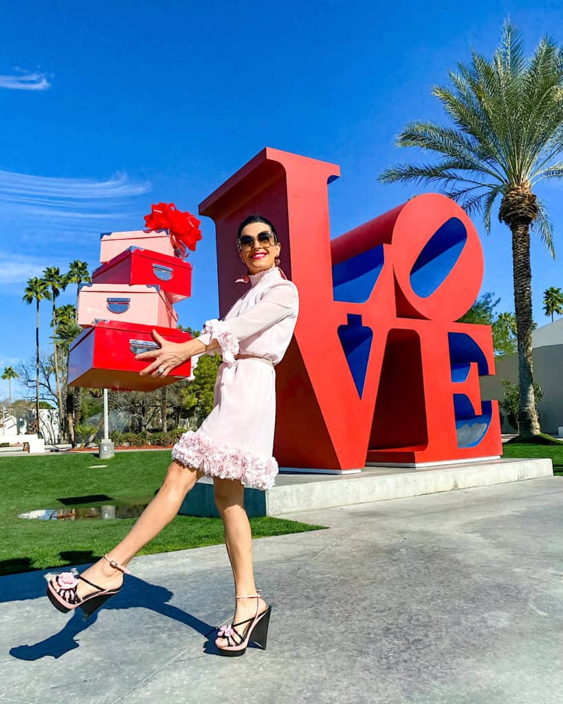 Woman in pink dress with gift boxes, LOVE sign in background. Valentine's day Gift Ideas. 