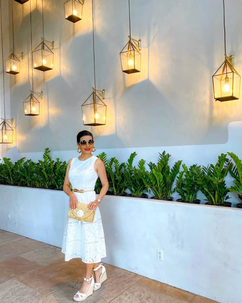 Woman wearing white dress, white wedge sandals and clutch bag