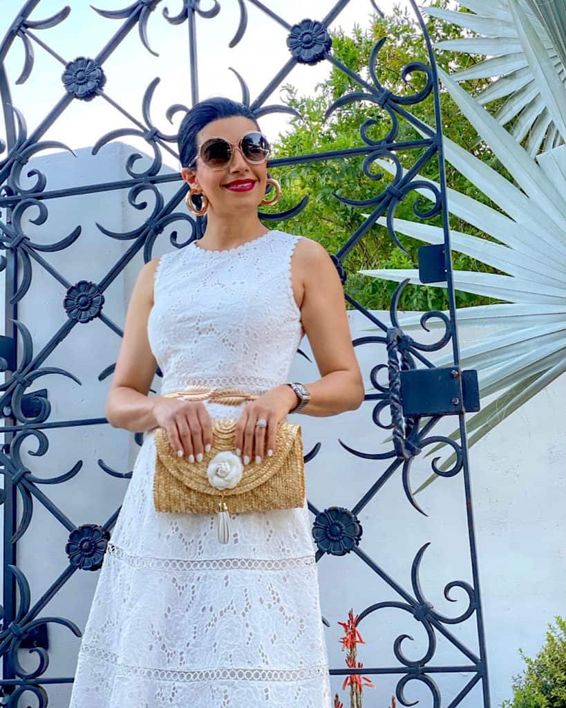 Woman leaning against blue gate wearing white dress and clutch bag