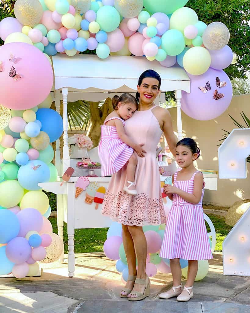 Mother and daughters beside ice cream cart and balloons. 