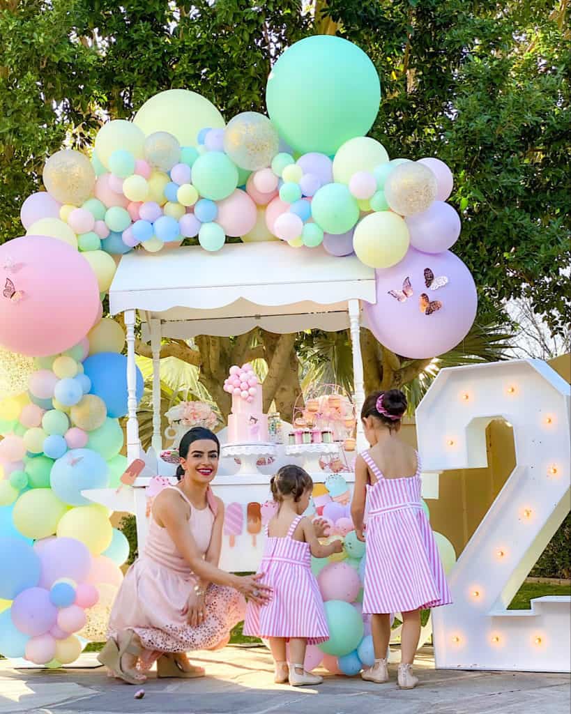 Mother and daughters beside ice cream cart, balloons and large lit up "2" sign. 