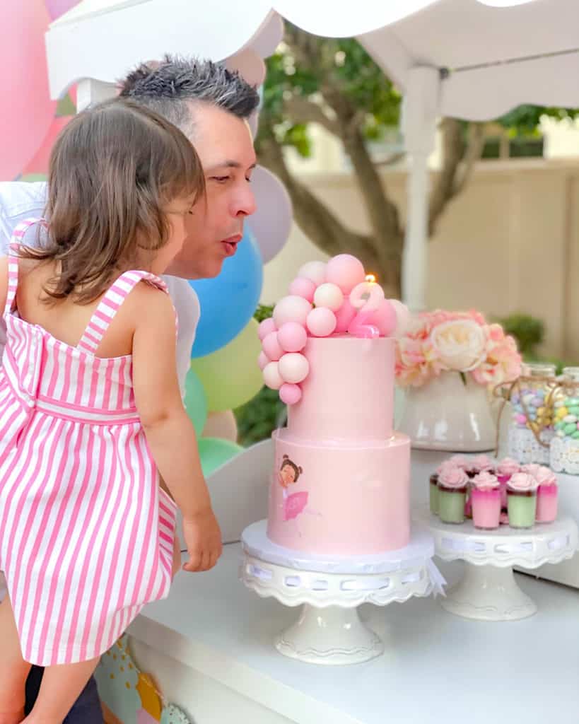 Girl and her dad blowing out birthday candle on Cinderella cake. 