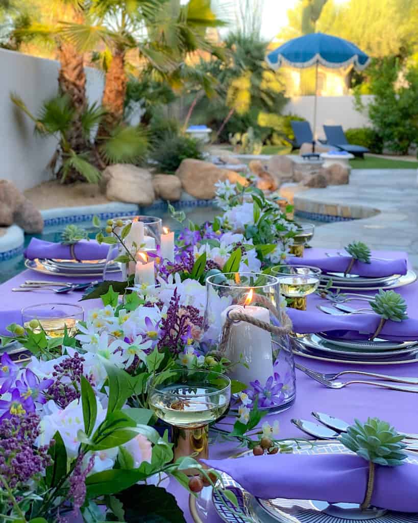 Flowers and candles and purple and green place settings on outdoor table.