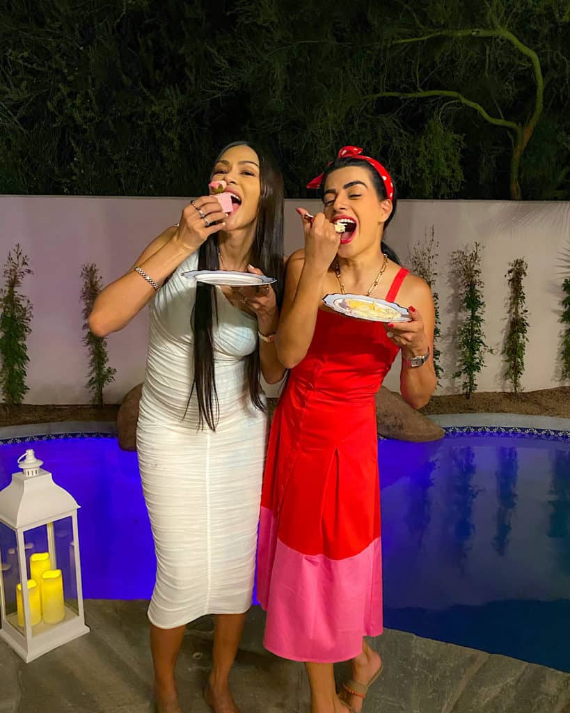 Expectant mother dressed in white with a woman in a red dresses eating cake 