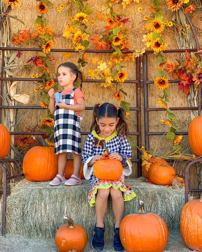 Cute Pumpkin Patch Outfit Ideas - 2 girls on a hay bale surrounded with fall decorations and pumpkins