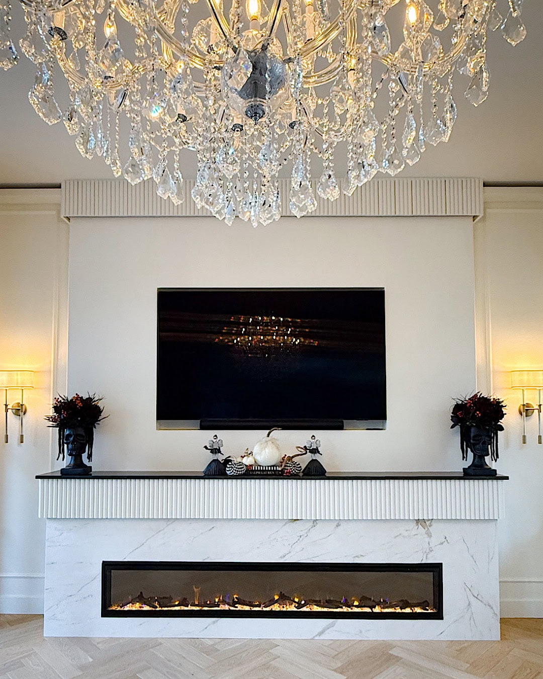 Halloween fireplace mantel with skull planters, pumpkins, and a crystal chandelier