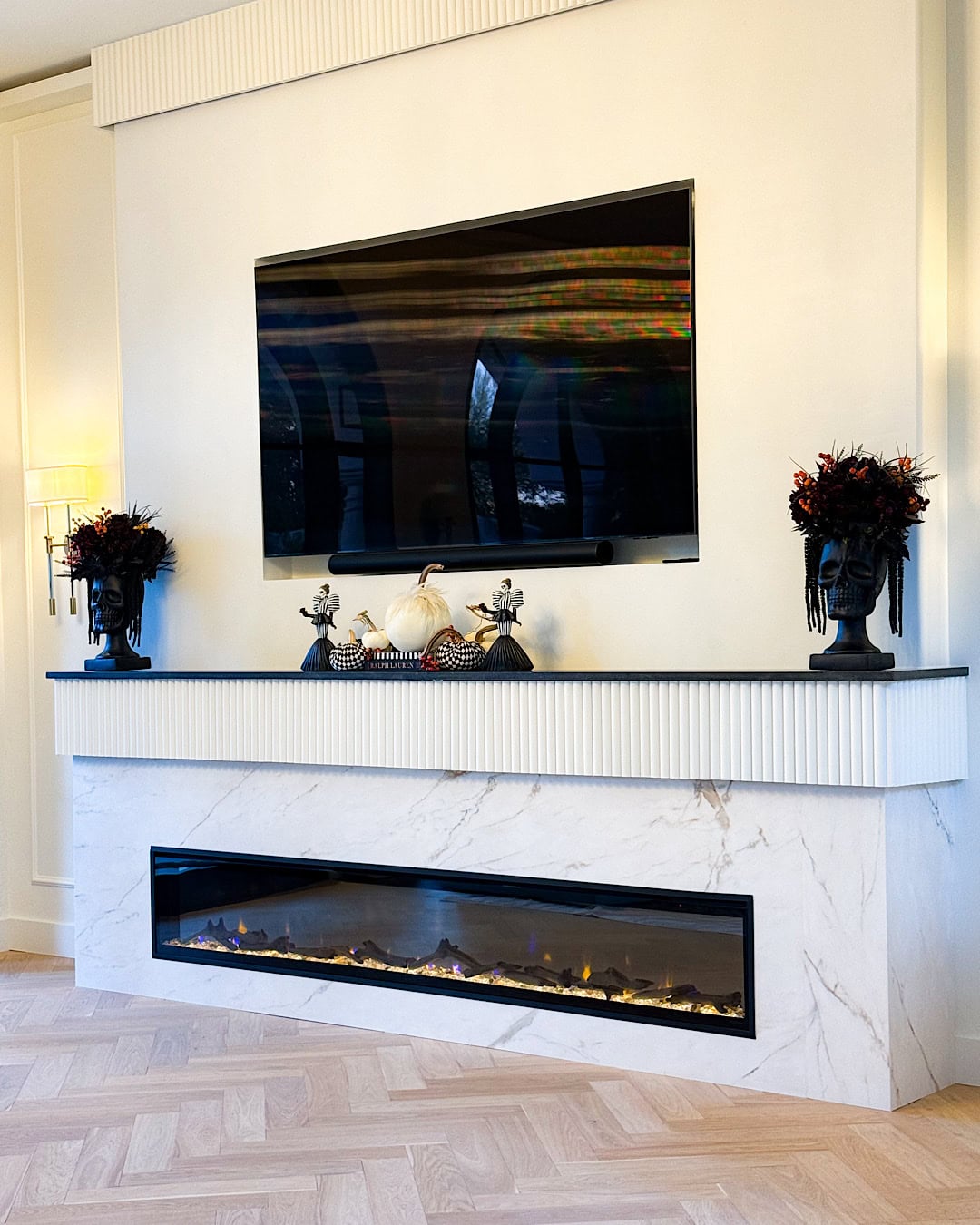 Halloween mantel decor with TV above a white marble fireplace