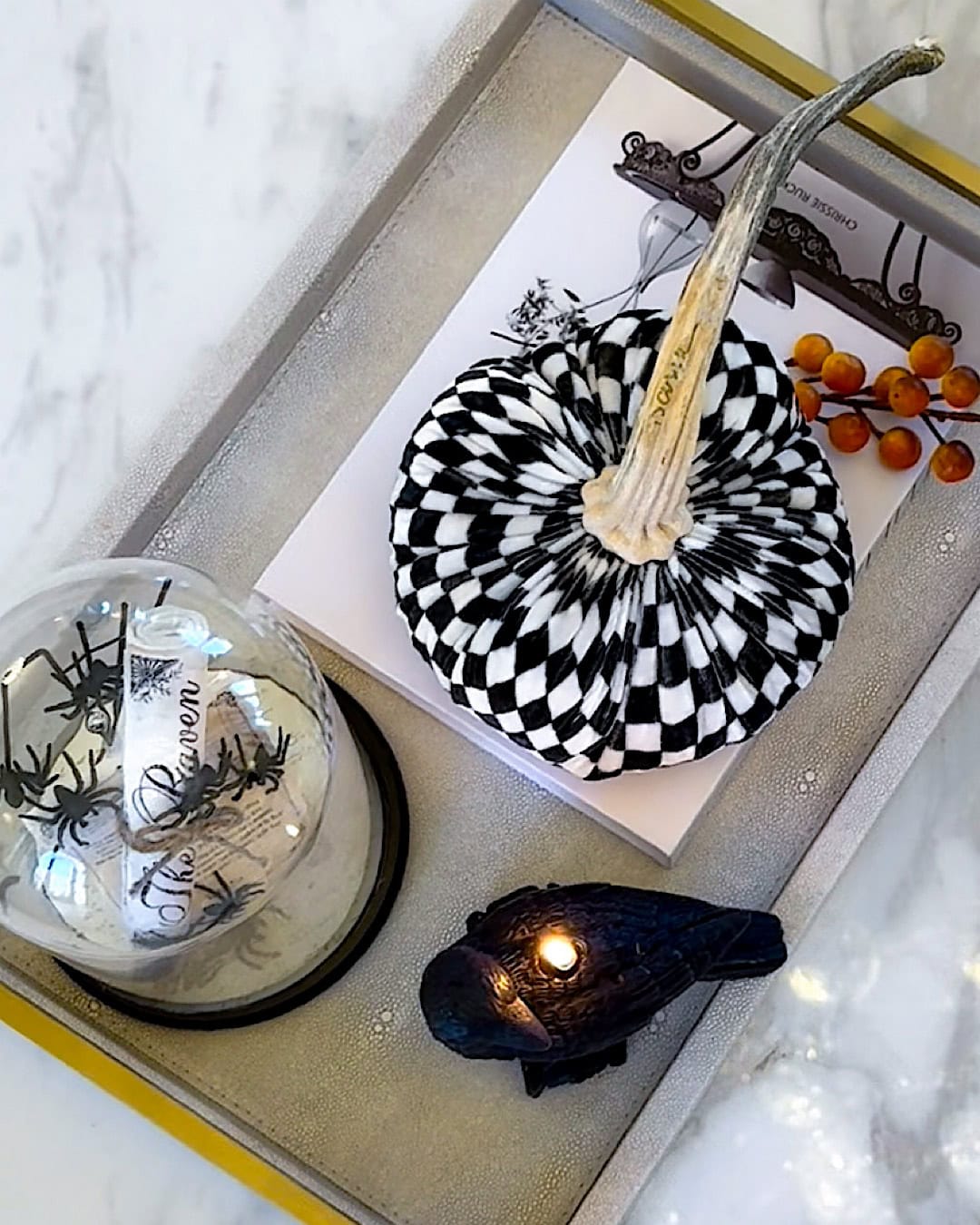 Halloween decorations on a coffee table tray with a checkered pumpkin, raven candle, and glass cloche