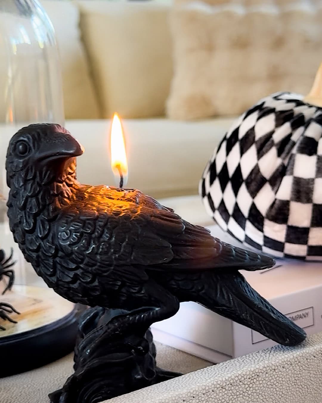 Spooky Halloween decor with a lit black raven candle and a checkered pumpkin